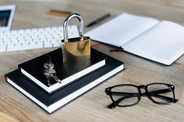 Padlock and keys on notebooks near eyeglasses and keyboard in office 