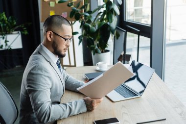 Asyalı sakallı işadamı ofiste dizüstü bilgisayarın yanında çalışıyor.