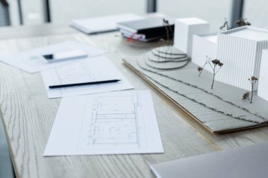 Bulanık defterler ve ahşap masadaki akıllı telefon yakınlarındaki ev modelleri ve planlar.