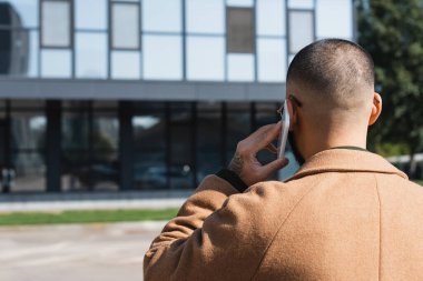Bej ceketli bir adamın şehir caddesinde cep telefonundan araması.