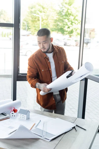 Arquitecto Asiático Mirando Papeles Mesa Trabajo Mientras Sostiene Plano Oficina — Foto de Stock