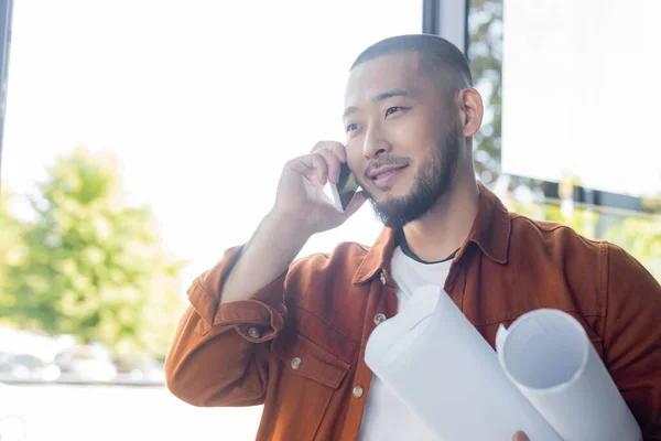 Happy Asian Architect Holding Rolled Blueprints While Talking Smartphone Office — Stock Photo, Image