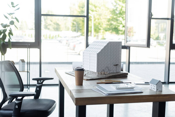 house models, documents and takeaway drink on desk in modern architectural agency