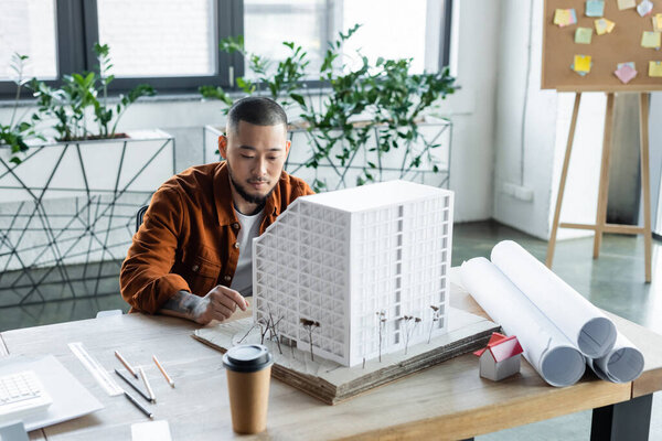 asian architect sitting near house model while working on architectural project in office