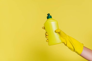 Plastik eldivenli, elinde deterjanı sarı olan temizleyicinin kısmi görüntüsü