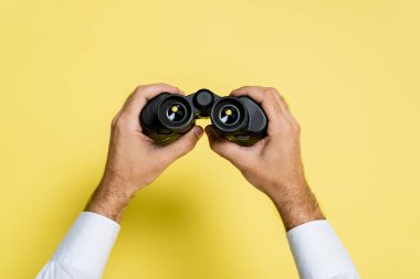 cropped view of man holding black binoculars in hands on yellow clipart