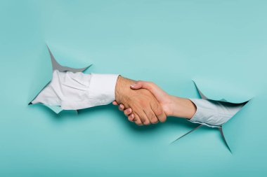Kırpılmış kadın ve erkeğin mavi duvardaki deliklerden el sıkışması görüntüsü