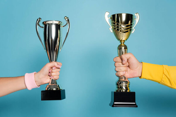 cropped view of man and woman holding golden and silver trophies on blue