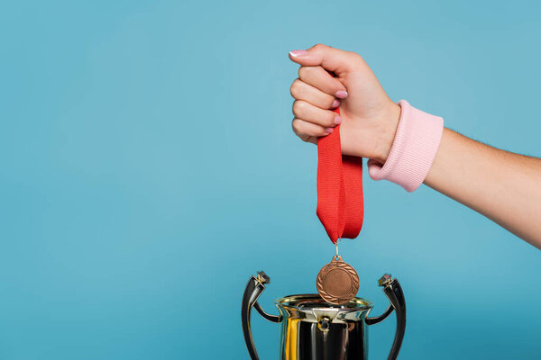 cropped view of sportswoman holding medal near golden cup isolated on blue