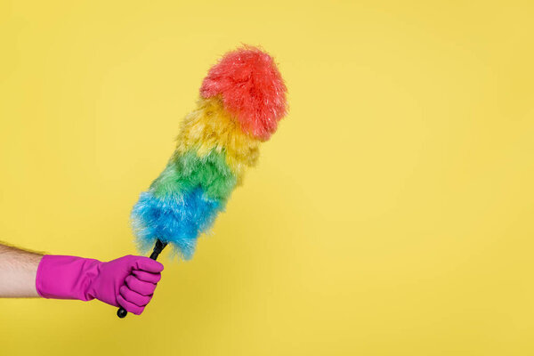partial view of man in rubber glove holding dust brush isolated on yellow
