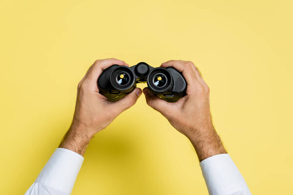 cropped view of man holding black binoculars in hands on yellow