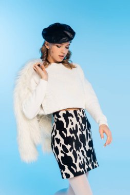 Bereli, etekli, beyaz kürk ceketli, mavi poz veren güzel bir kadın.