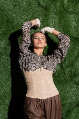 Çimenli arka plana dayanan zebra desenli, korseli ve eldivenli genç model. 