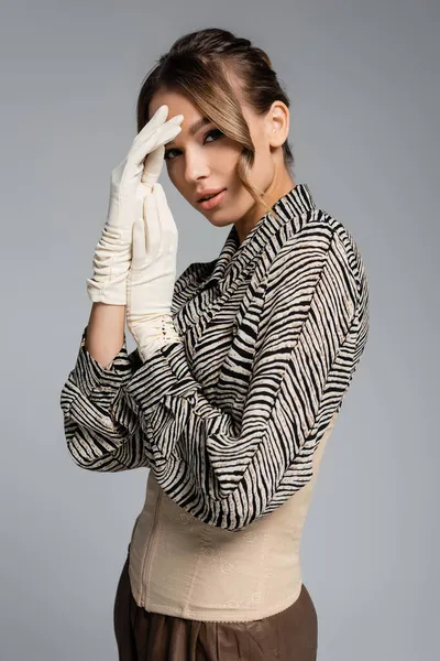 young woman in blouse with animal print and white gloves posing isolated on grey