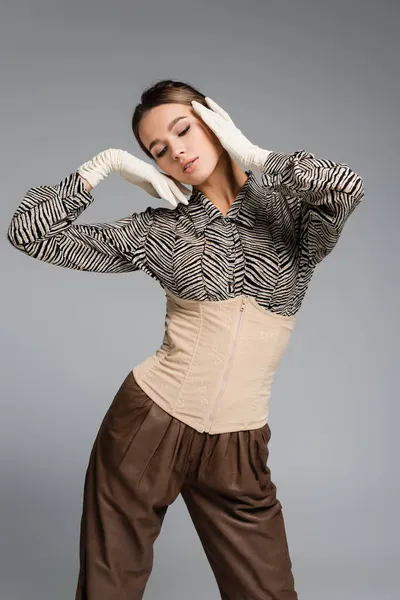 trendy woman in blouse with animal print, gloves and corset posing isolated on grey