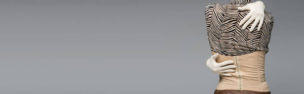 обрезанный вид женщины в блузке с животным шрифтом, перчатками и корсетом обнимающей себя изолированной на сером, баннер