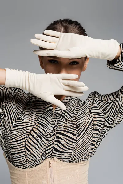 stylish woman in blouse with zebra print and white gloves posing isolated on grey