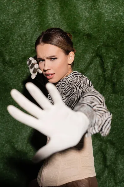 young trendy model in blouse with zebra print and gloves showing no gesture near grassy background