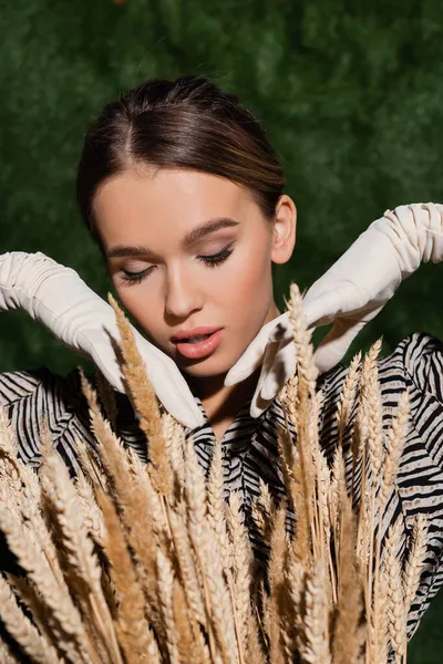 trendy young model in blouse with animal print and white gloves posing near wheat spikelets