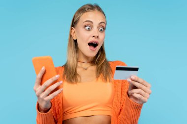 Heyecanlı sarışın kadın elinde kredi kartı ve akıllı telefon tutuyor. 