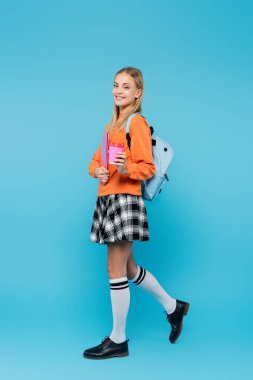 Sırt çantalı gülümseyen bir öğrenci dizüstü bilgisayar ve kahve taşıyor. 