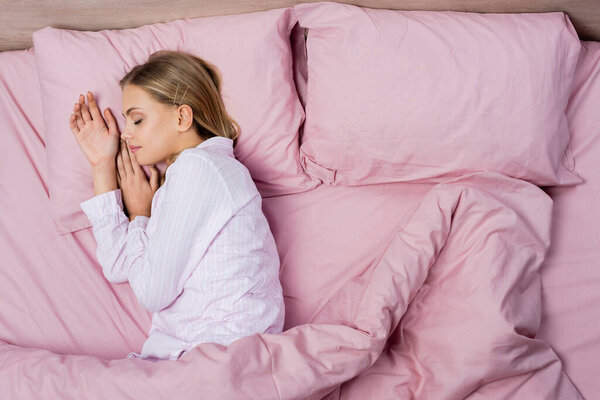 Top view of woman in pajamas sleeping on pink bedding at home