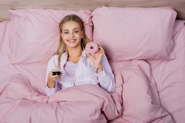 Vista Superior Mujer Positiva Sosteniendo Mando Distancia Donut Cama — Foto de Stock