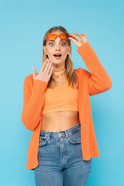 Excited blonde woman in sunglasses looking at camera isolated on blue 