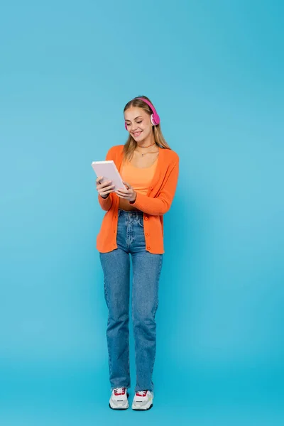 Positieve Vrouw Hoofdtelefoon Houden Notebook Terwijl Staan Een Blauwe Achtergrond — Stockfoto