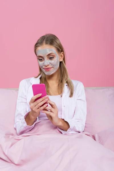 Mujer Rubia Con Máscara Arcilla Cara Usando Teléfono Inteligente Cama — Foto de Stock