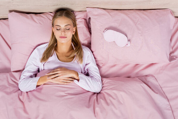 Top view of blonde woman sleeping near mask on bed 