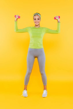 Gri taytlı, yeşil uzun kollu tişörtlü, sarı halterli bir kadın.