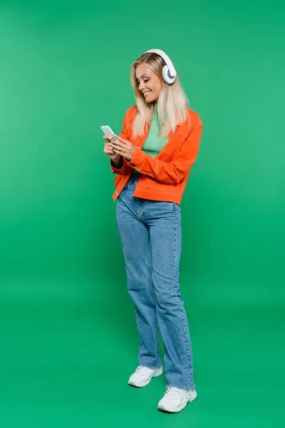 Άποψη Πλήρους Μήκους Της Ευτυχούς Γυναίκας Στα Ακουστικά Χρησιμοποιώντας Smartphone — Φωτογραφία Αρχείου