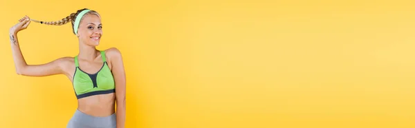 Веселая Спортивная Женщина Держит Волосы Улыбаясь Камеру Изолированы Желтый Баннер — стоковое фото