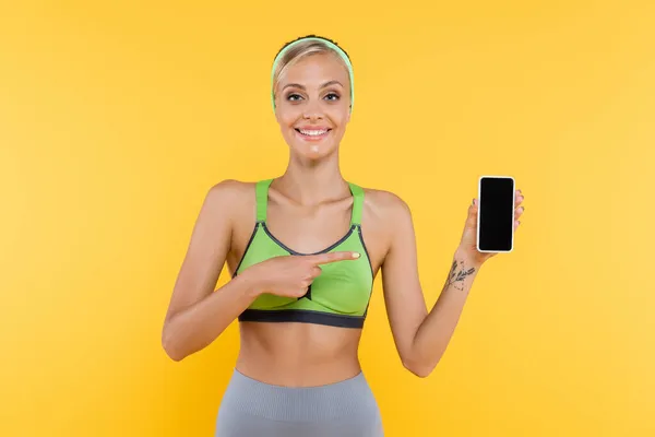 Радостная Женщина Спортивной Одежде Указывающая Мобильный Телефон Пустым Экраном Изолированным — стоковое фото