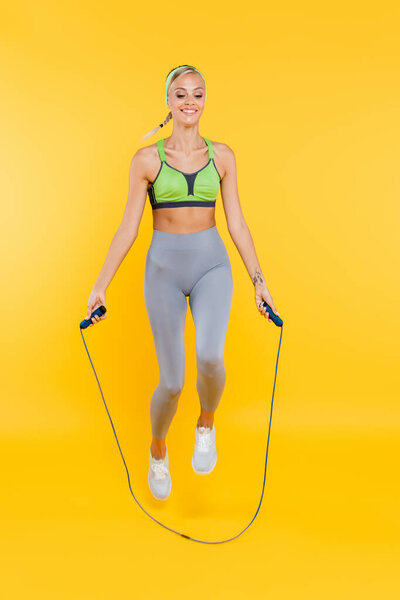 Вид в полный рост счастливой женщины в серых ногах и зеленом спортивном бюстгальтере, прыгающей с трамплина на желтом