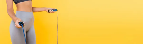 黄色のバナーに隔離されたジャンプロープを保持グレーのレギンスでスポーツ女性のクロップドビュー — ストック写真