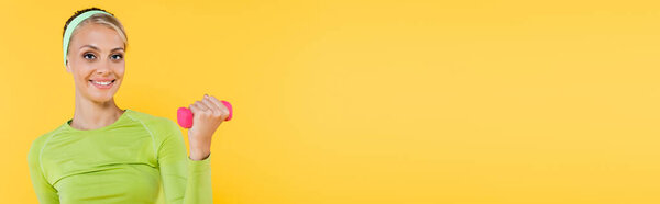 pretty woman looking at camera while working out with dumbbell isolated on yellow, banner