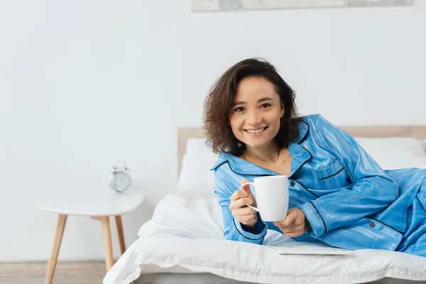 穿着蓝色睡衣的快乐的年轻女人在家里喝茶 — 图库照片