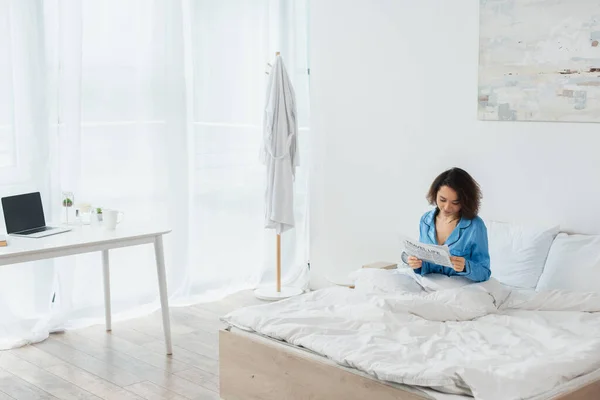 Brunette Woman Blue Pajamas Reading Travel Life Newspaper Bed Laptop — Stock Photo, Image