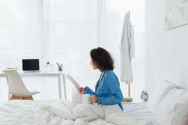 Cheerful Woman Blue Pajamas Reading Newspaper Holding Cup Bed — Stock Photo, Image