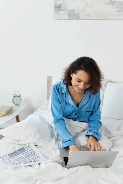 Sorrindo Jovem Mulher Pijama Usando Laptop Perto Jornal Cama — Fotografia de Stock