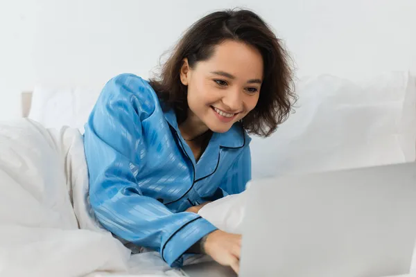 穿着睡衣的年轻自由职业者在卧室里用笔记本电脑微笑 — 图库照片