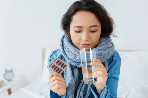 病気の若い女性ニットスカーフ保持ガラスの水とブリスターパックで丸薬 — ストック写真