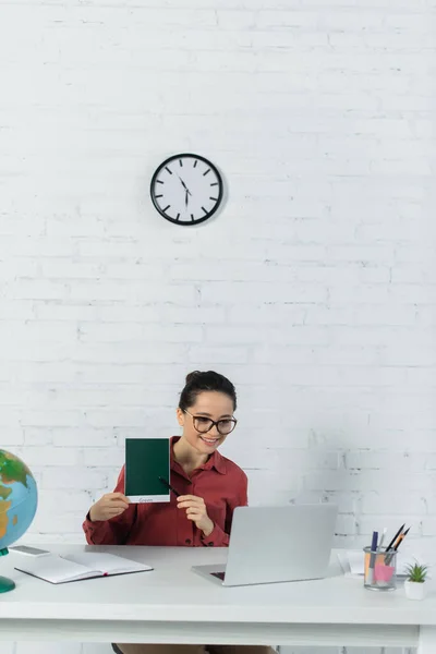 Cheerful Teacher Eyeglasses Holding Card Green Lettering Looking Laptop Globe — Stock Photo, Image