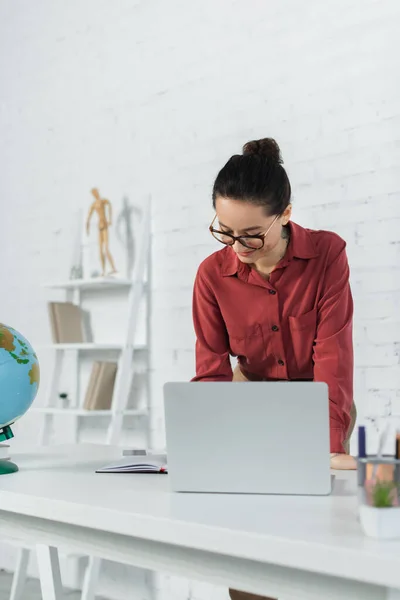 Smiling Teacher Eyeglasses Looking Notebook Globe Devices Desk — Stock Photo, Image