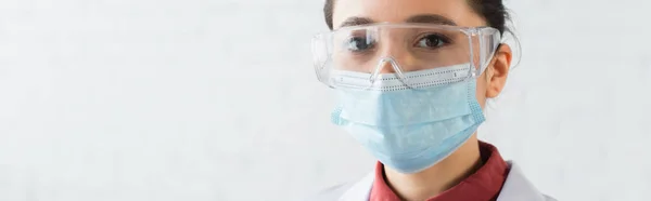 穿着护目镜和医疗面罩在实验室看着相机的黑发科学家 — 图库照片