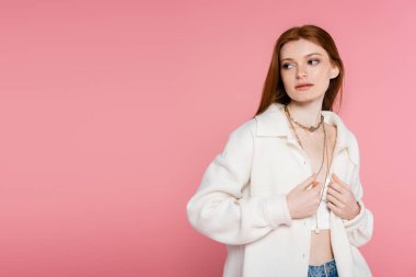 Güzel kızıl saçlı kadın pembeye bürünmüş ceketini düzeltiyor.