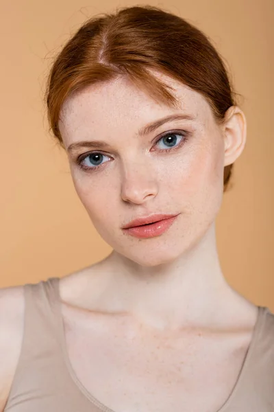 Portrait of young redhead woman with freckles looking at camera isolated on beige