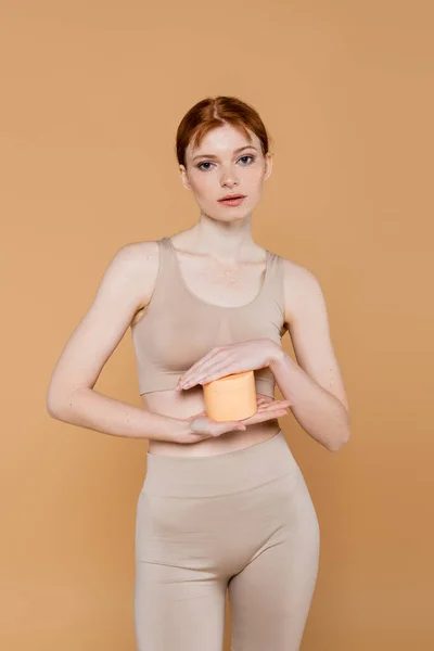 红头发的女人拿着用米黄色隔离的奶油制成的容器 — 图库照片
